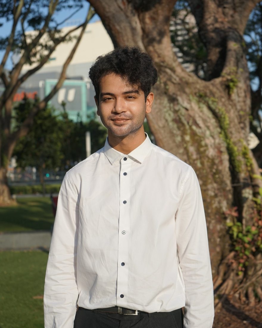 Vishal Venkatagiri, smiling, in a white shirt in front of a large tree